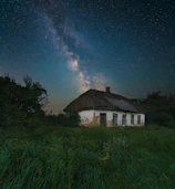 A traditional Bhutanese house framed by the Milky Way stretching across the night horizon.