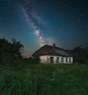 A traditional Bhutanese house framed by the Milky Way stretching across the night horizon.