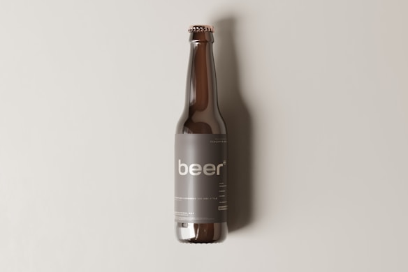A brown glass beer bottle with a minimalist label design that prominently features the word 'beer' in lowercase letters. The bottle is standing upright against a plain, light beige background, casting a soft shadow to the right.