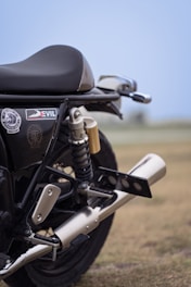 A close-up view of a motorcycle's rear section, highlighting the black seat and suspension system. The exhaust pipe is prominently featured, with a label saying 'Devil' visible on the side panel. The background is blurred, suggesting an outdoor setting.