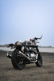 A vintage motorcycle parked beside a rustic barn under a clear blue sky.