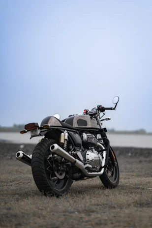 A vintage motorcycle parked beside a rustic barn under a clear blue sky.