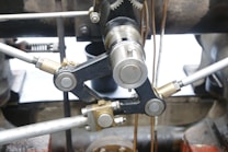 Close-up view of a metal mechanical component with interconnected rods and cylindrical gears, featuring metallic surfaces with various finishes, surrounded by industrial machinery parts.