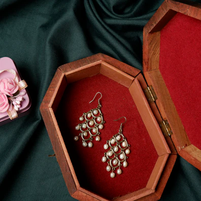 A sleek black velvet jewelry box open to reveal a pair of pearl drop earrings.