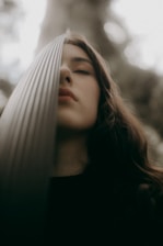 A person with closed eyes leans against a textured vertical surface, creating a tranquil and introspective atmosphere. The textured surface partially obscures the face, and soft, natural lighting enhances the serene mood.