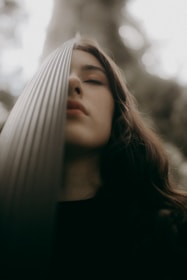 A person with closed eyes leans against a textured vertical surface, creating a tranquil and introspective atmosphere. The textured surface partially obscures the face, and soft, natural lighting enhances the serene mood.