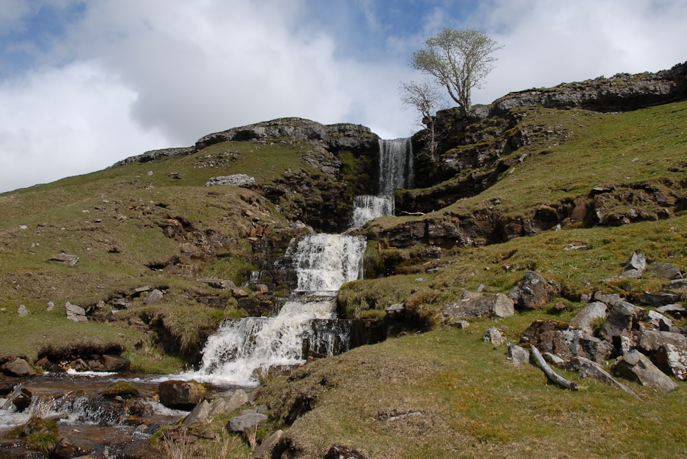 a small waterfall in the middle of a grassy hill