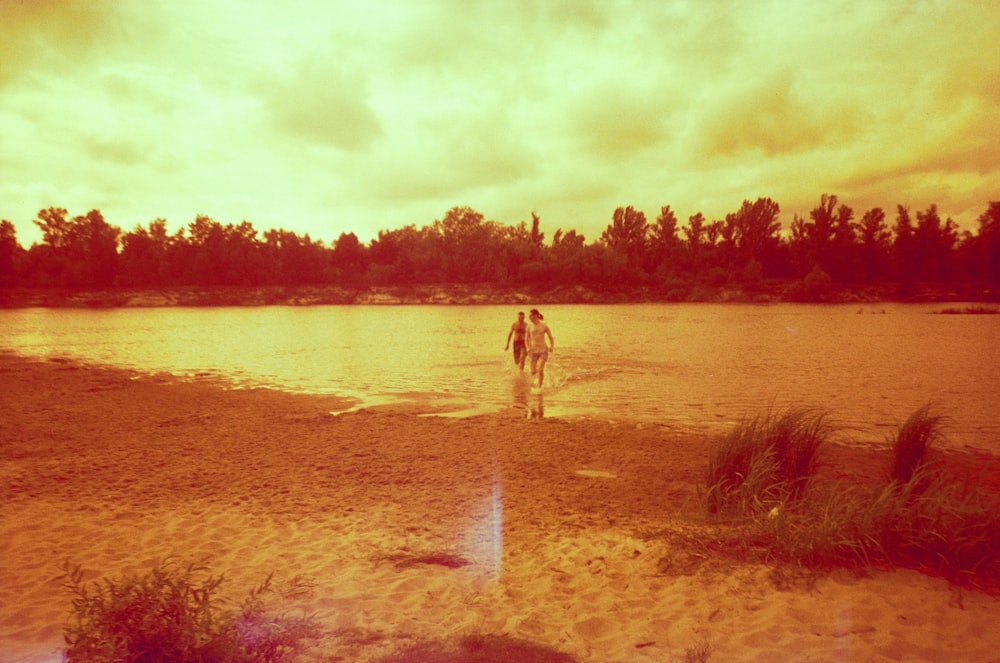 a couple of people standing on top of a sandy beach