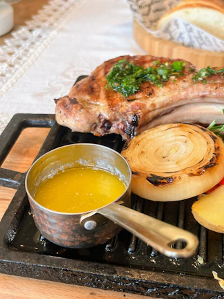 A sizzling grilled pork chop with herbs and lemon on a rustic wooden board.