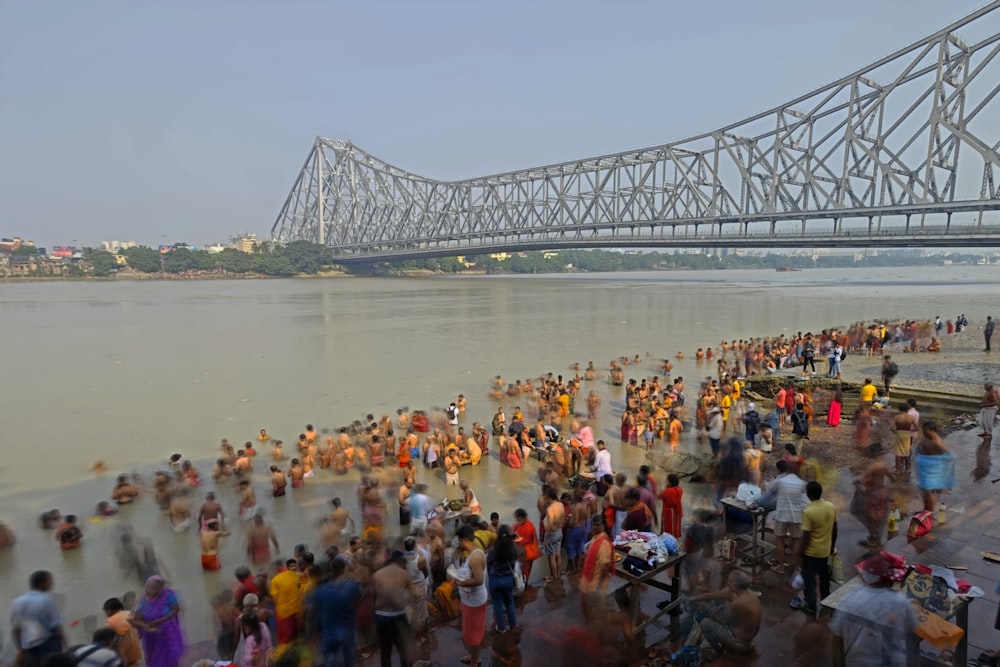 a crowd of people standing on a beach next to a bridge