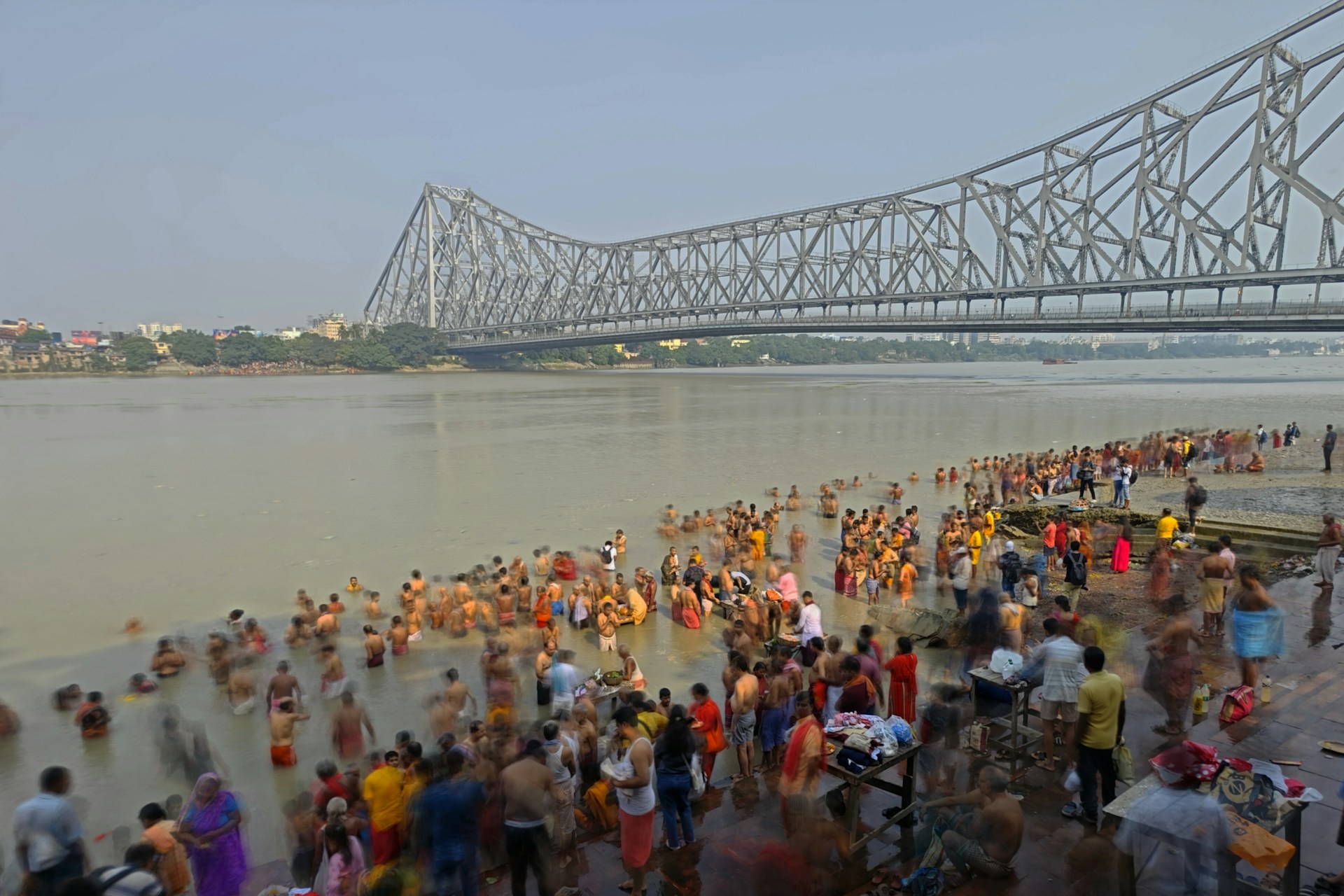 a crowd of people standing on a beach next to a bridge