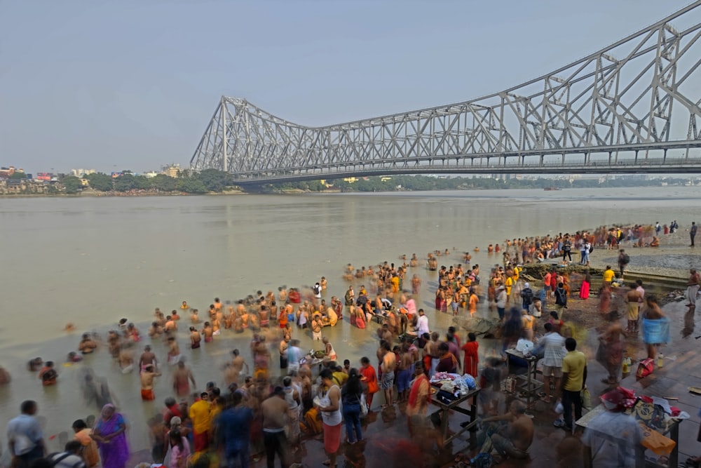 una multitud de personas de pie en una playa junto a un puente