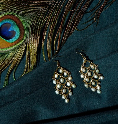 Close-up of a pair of blue gold feather earrings resting on a soft velvet cloth, highlighting the delicate feathers and shimmering semi-precious stones.