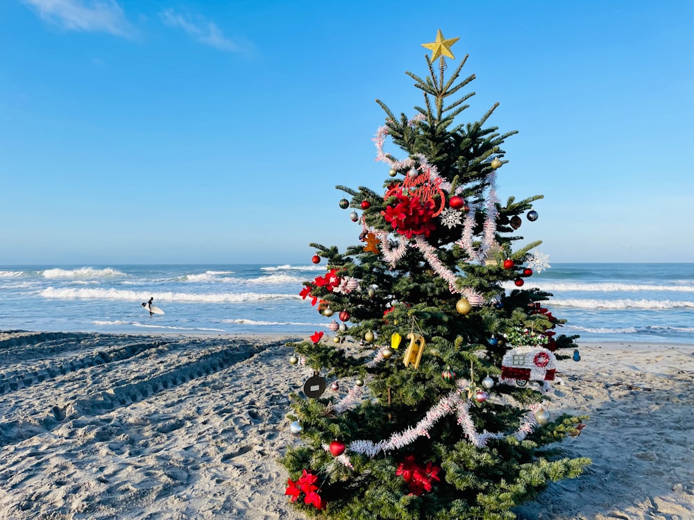 Un albero di Natale sulla spiaggia con una tavola da surf sullo sfondo