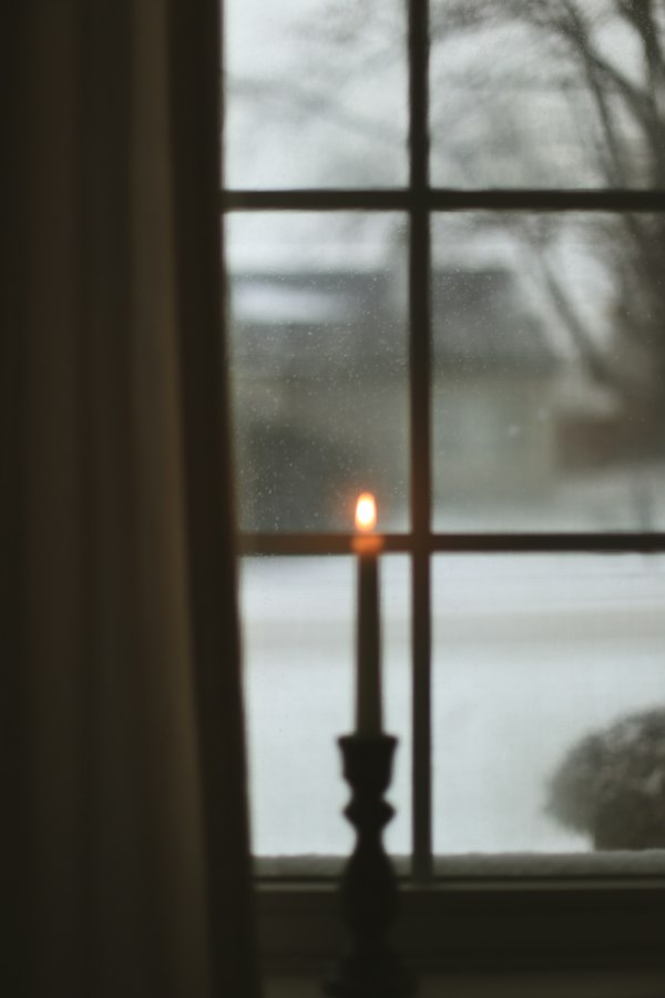 A single lit candle glowing in front of a softly lit window