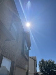 A professional inspector carefully examining the exterior of a residential home under clear daylight.