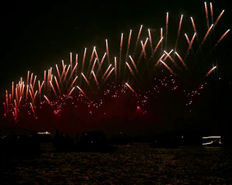 A close-up of sparkling fireworks launching into the night sky above a beautifully decorated wedding venue.