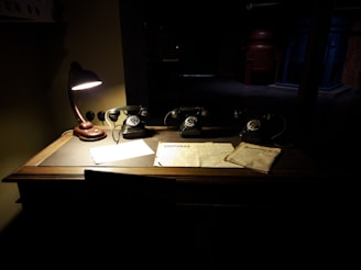 A warmly lit antique desk with a vintage telephone and a stack of art catalogues.