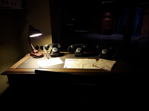 A warmly lit antique desk with a vintage telephone and a stack of art catalogues.