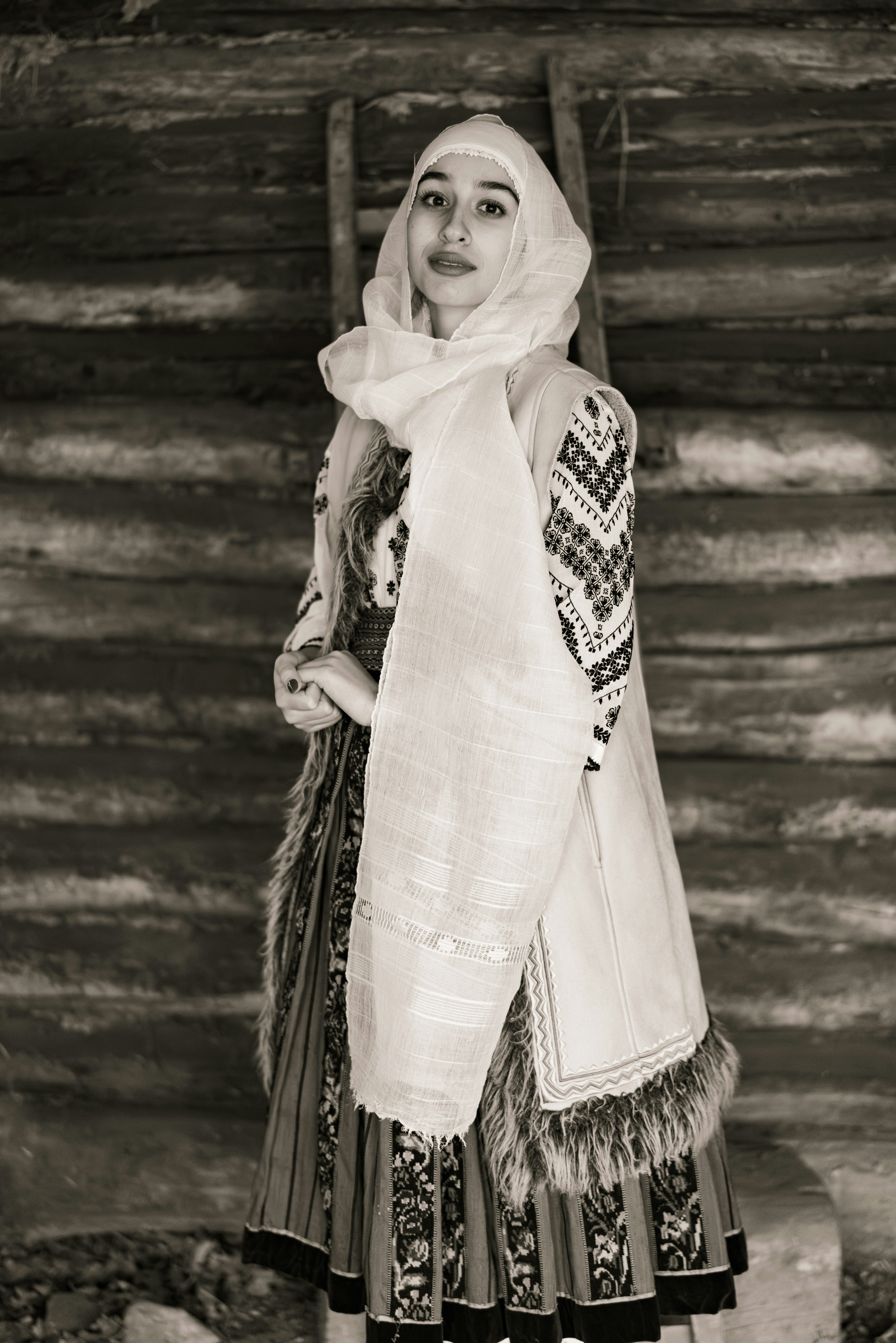 une femme en robe et foulard debout devant une cabane en rondins