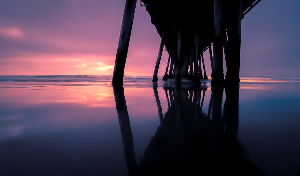 the sun is setting at the end of a pier