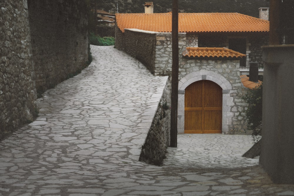 a cobblestone street with a stone building and orange tiled roof