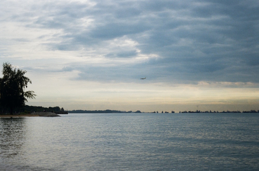 a plane flying over a body of water under a cloudy sky