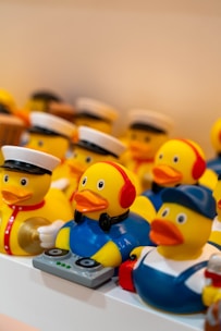 A collection of rubber duck toys, each styled in unique costumes. One duck is dressed as a DJ with headphones and a mixing console, while others are dressed as sailors and workers with hats.