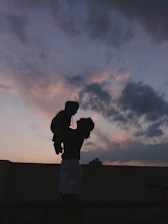 An eerie silhouette of a young mother holding a baby against a twilight sky.