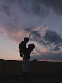 An eerie silhouette of a young mother holding a baby against a twilight sky.