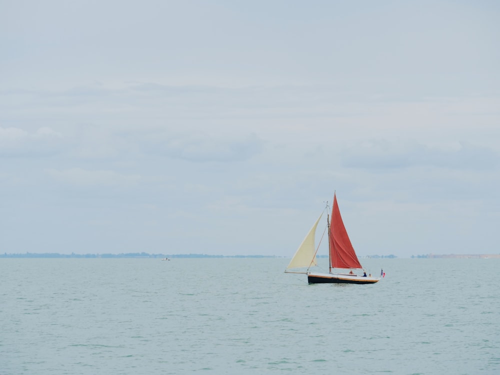 a sailboat with a red sail is in the middle of the ocean