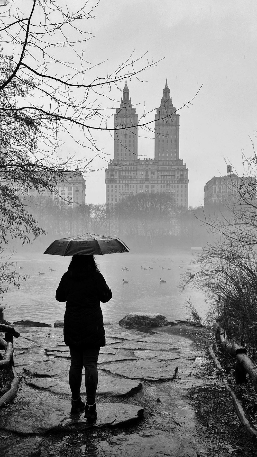 eine Person mit einem Regenschirm, die auf einem Weg in der Nähe eines Gewässers steht