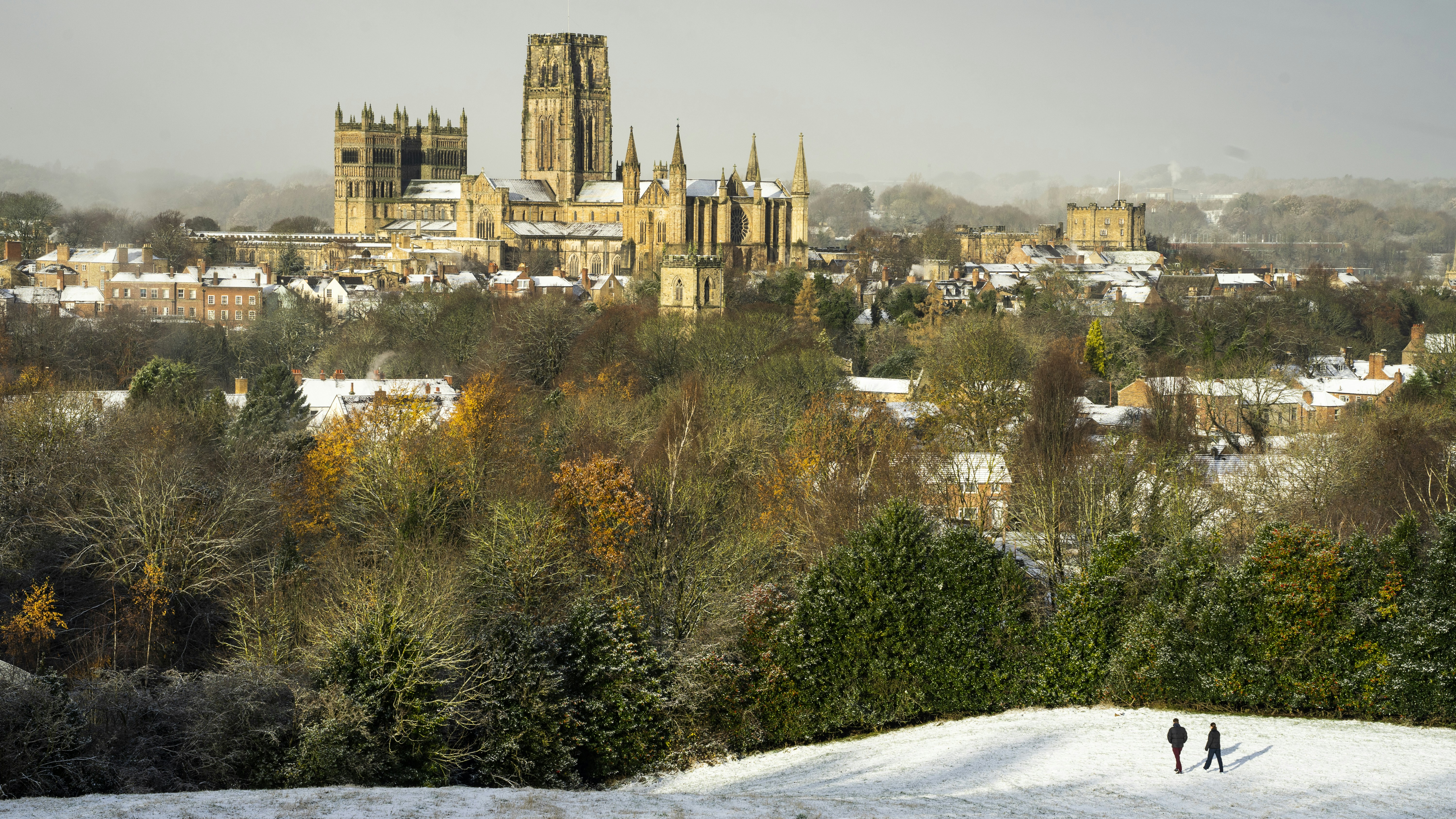 two people walking in the snow in front of a city
