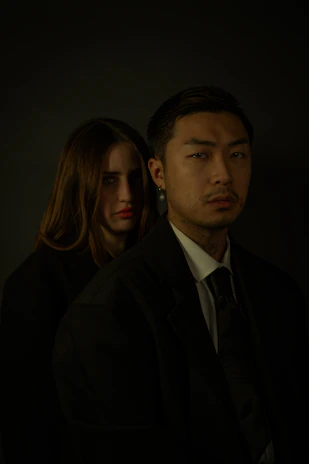 A moody black-and-gold cinematic shot of a masked couple in a dimly lit luxury suite, their silhouettes blending into dark elegant gradients.