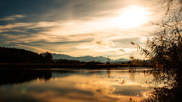 A serene landscape with a calm lake reflecting the mountains at sunrise.