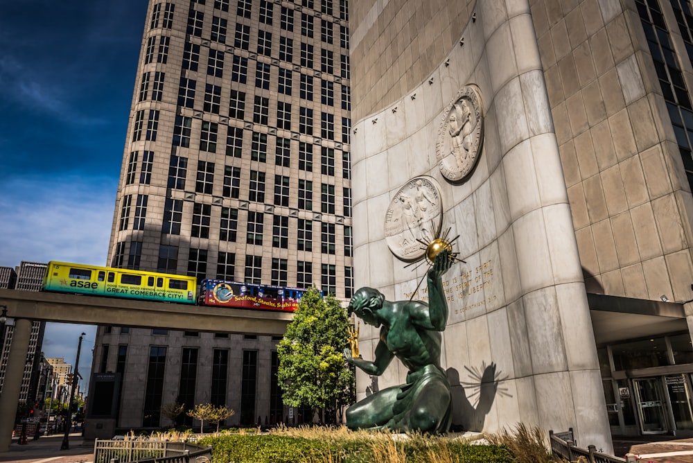 una estatua frente a un edificio con un tren pasando