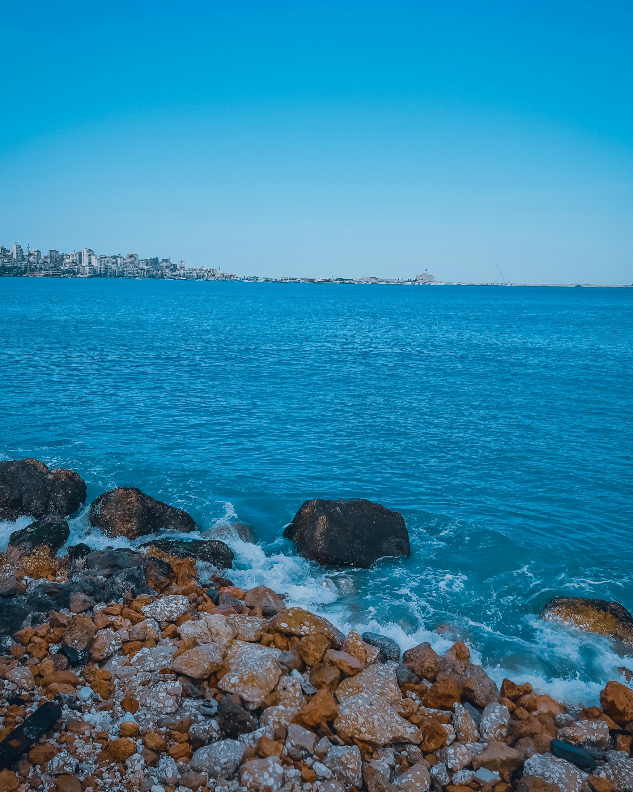 A body of water with rocks in the foreground and a city in the ...