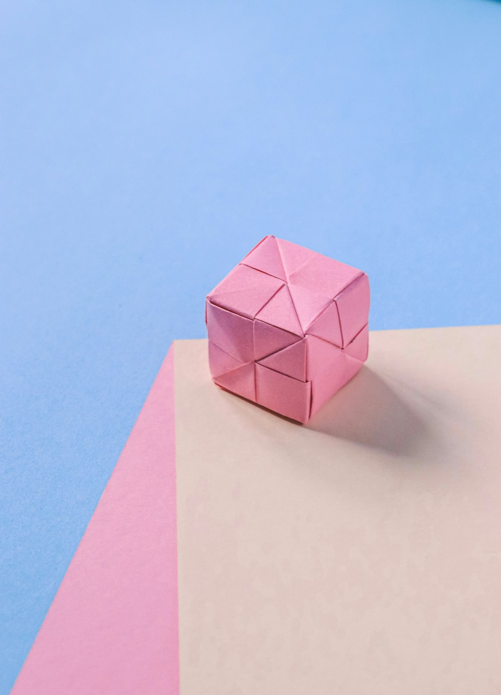 a pink origami object sitting on top of a blue and pink surface