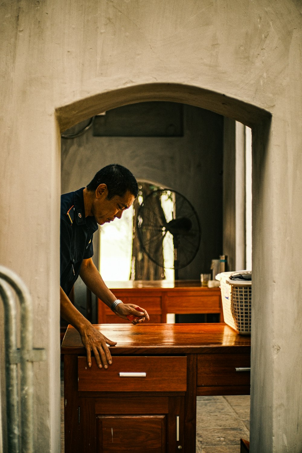 a man leaning over a wooden desk with a clock in the background