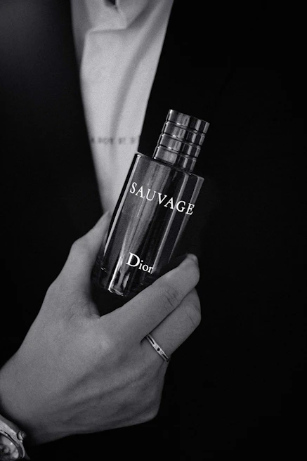 A candid shot of a man in a tailored black suit, holding a Vesario Desire bottle with a subtle smile.