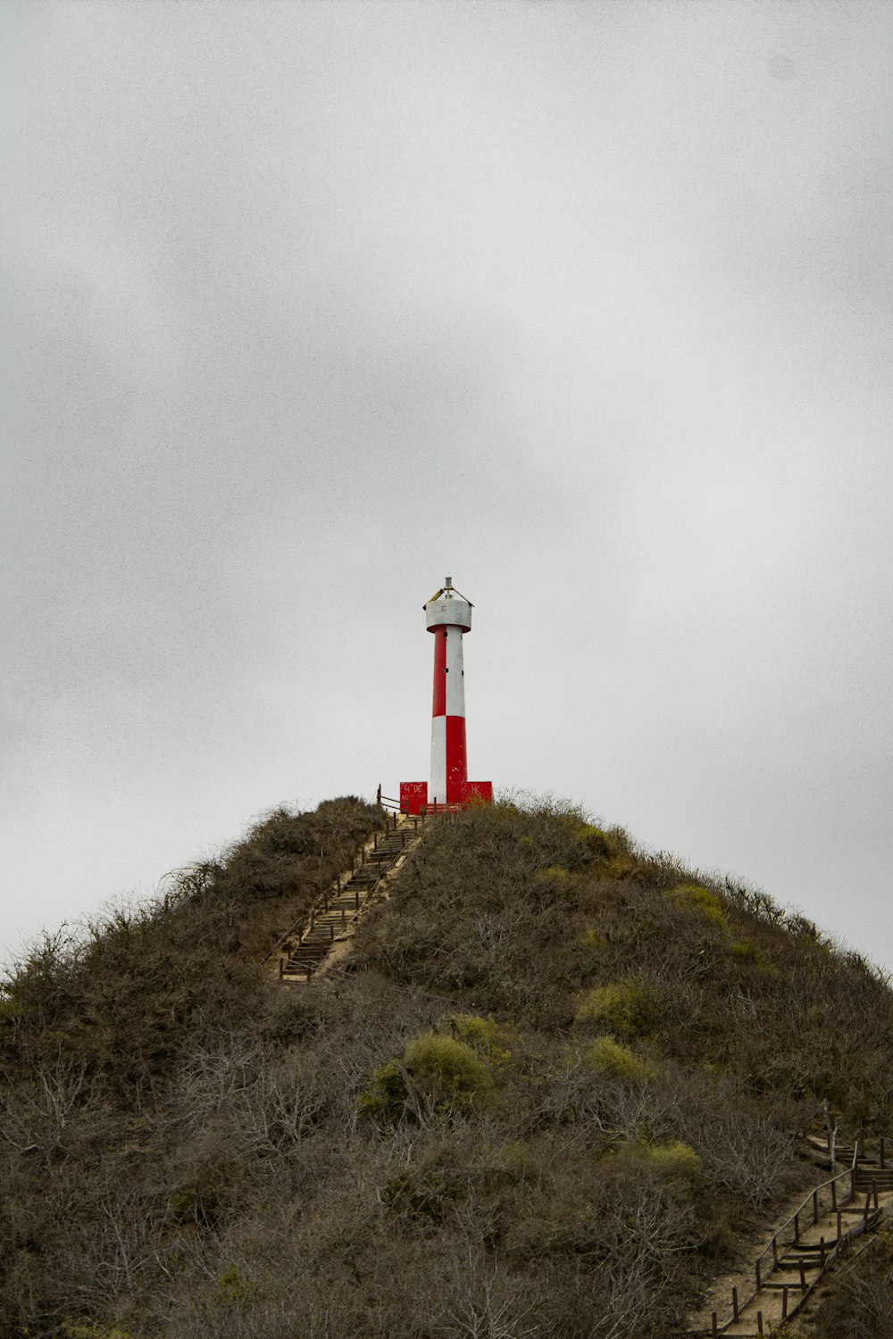 um farol vermelho e branco no topo de uma colina