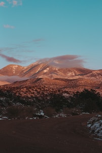 A sunlit mountain trail winding through golden fields under a clear blue sky, inviting travelers to embark on an epic adventure.