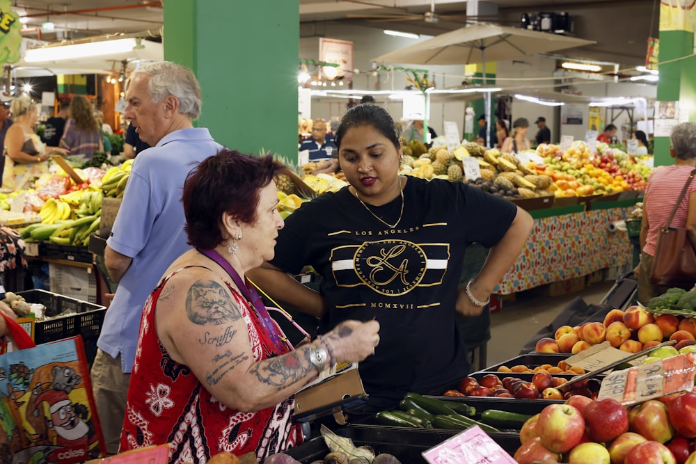 un groupe de personnes debout autour d’un stand de fruits et légumes