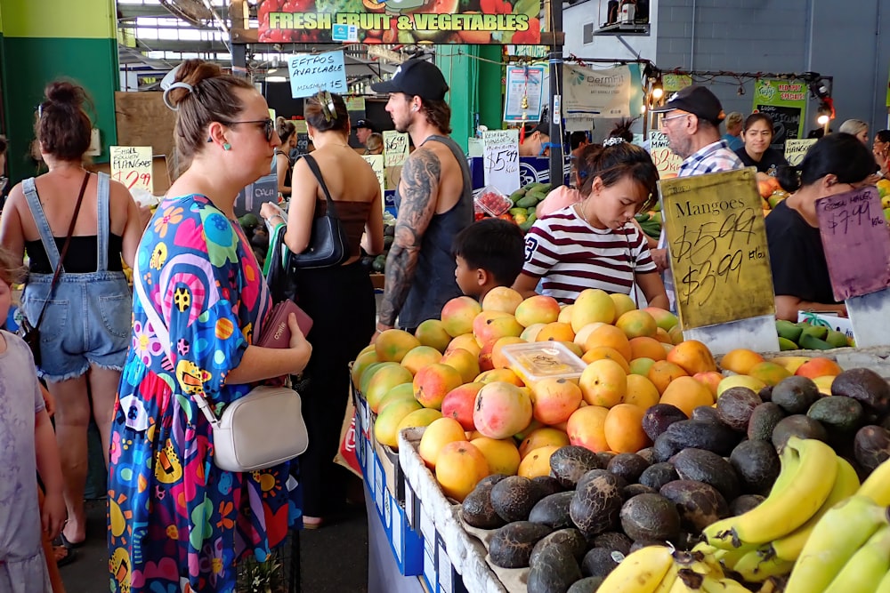 un groupe de personnes debout autour d’un étal de fruits