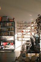 A warmly lit stationery shop interior features shelves lined with books and colorful bags, a display of greeting cards arranged on the wall, and various stationery items organized neatly. Sunlight casts soft shadows across the floor.