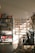 A warmly lit stationery shop interior features shelves lined with books and colorful bags, a display of greeting cards arranged on the wall, and various stationery items organized neatly. Sunlight casts soft shadows across the floor.