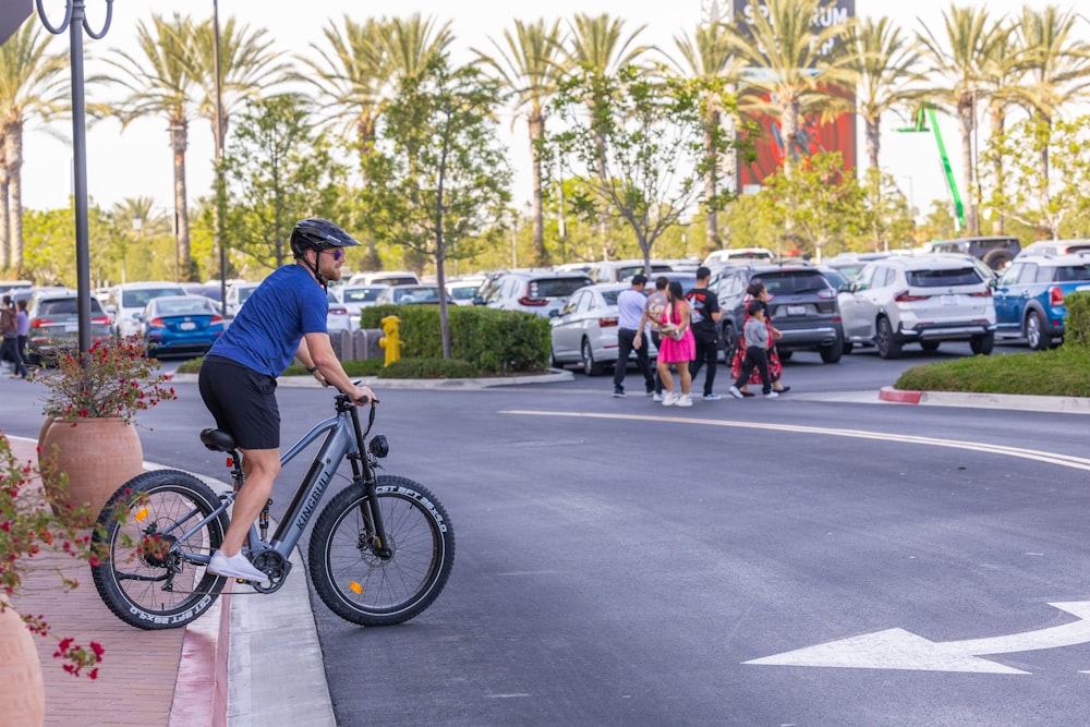 a man riding a bike down a street next to a parking lot