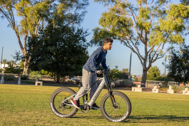 A happy customer riding a blue electric bike through a leafy park on a sunny day.