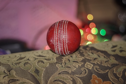 Close-up of a vibrant football and cricket ball resting on a stadium turf under bright lights.