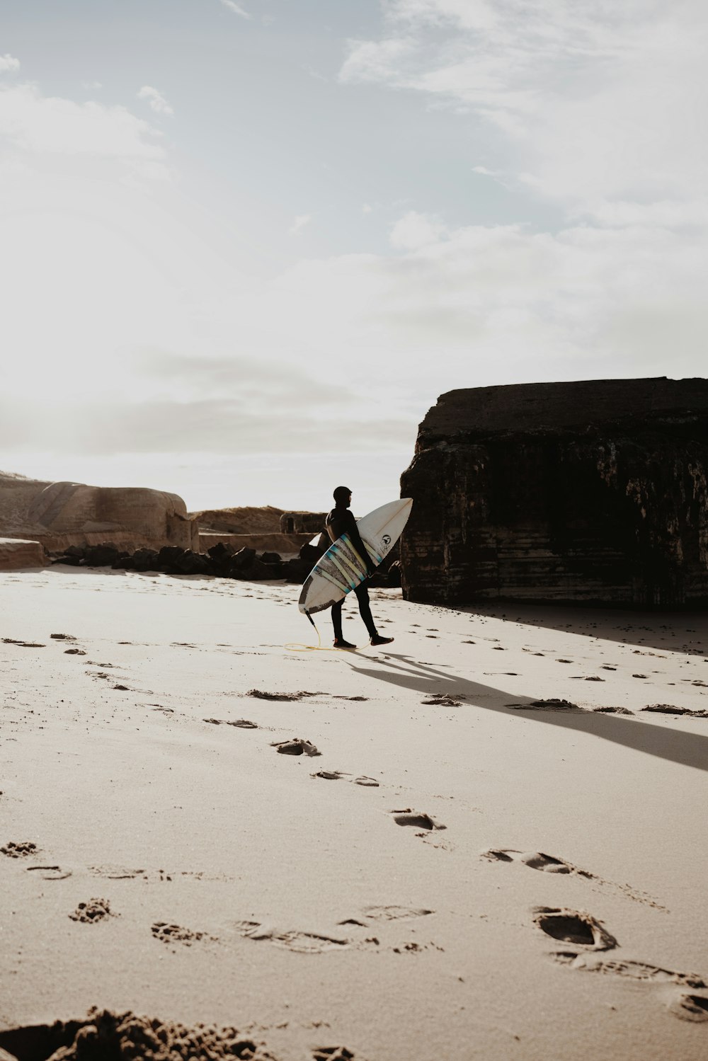 eine Person, die mit einem Surfbrett am Strand spazieren geht